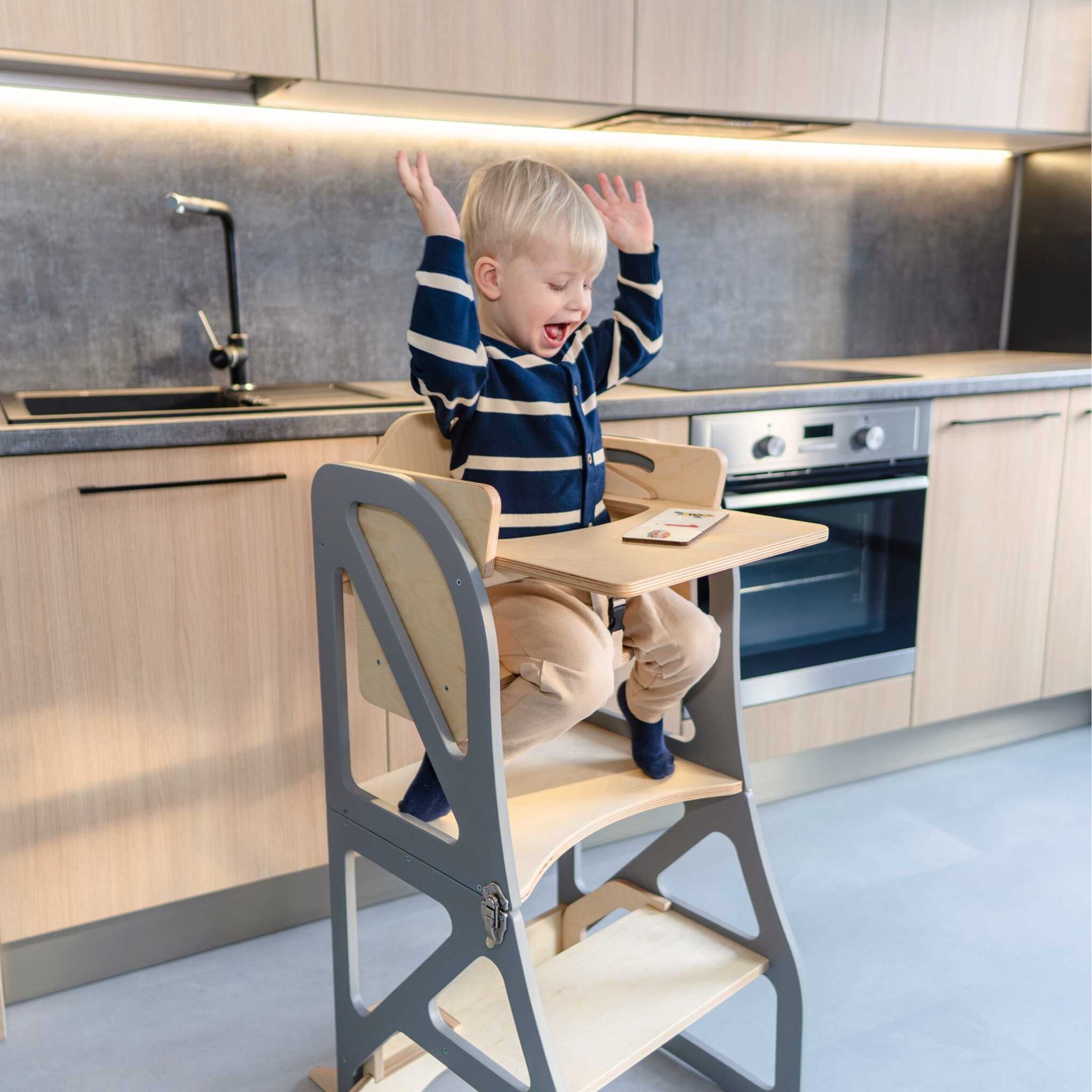Child using a transformable kitchen tower with high chair and tray add-on at the kitchen counter