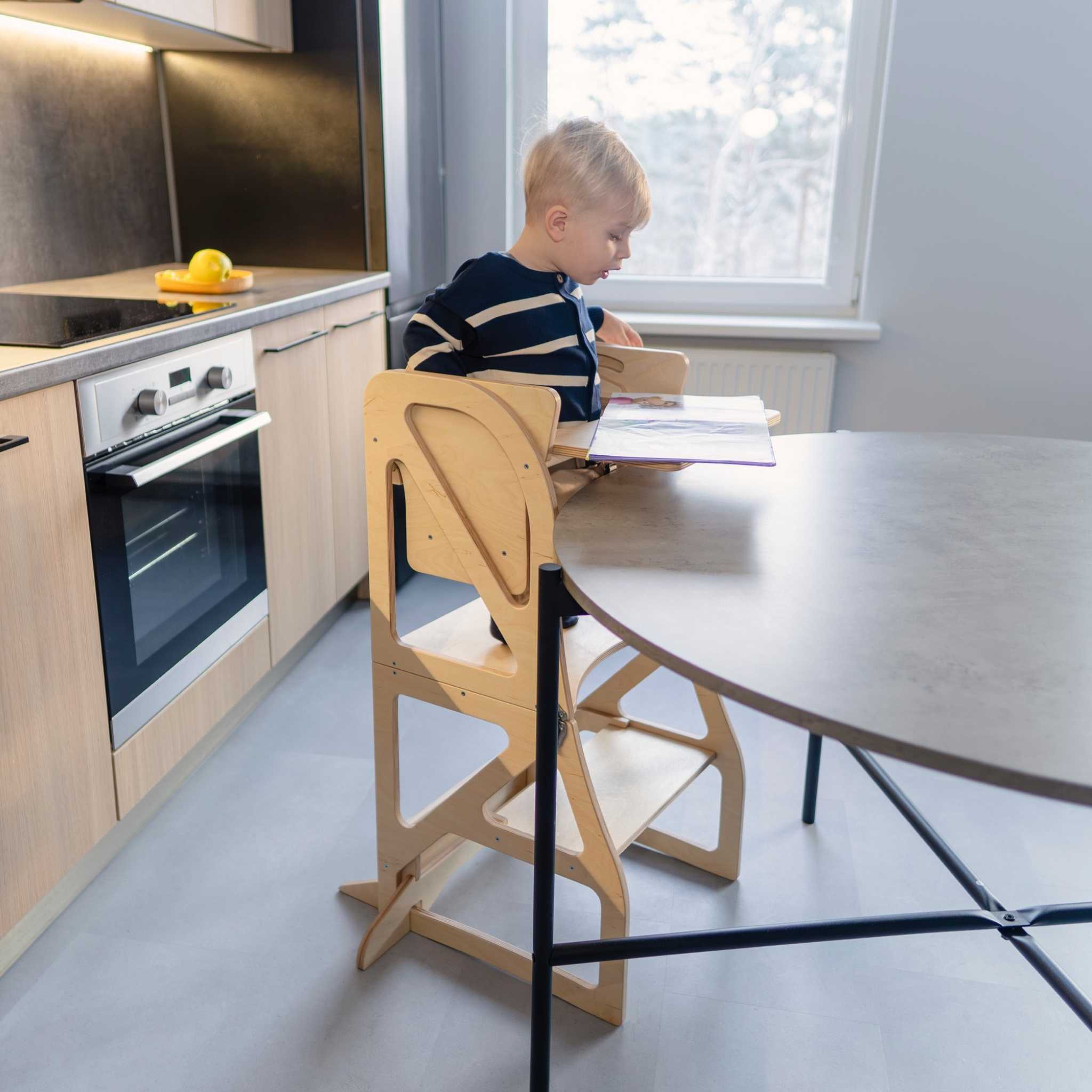 Child sitting at the kitchen table inside a transformable kitchen tower, using the high chair and tray add-on combo