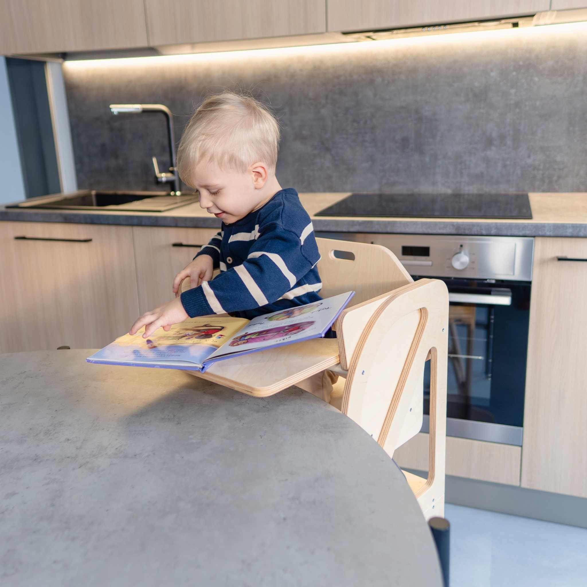 Child using a transformable kitchen tower with high chair and tray add-on for drawing and play at the kitchen counter