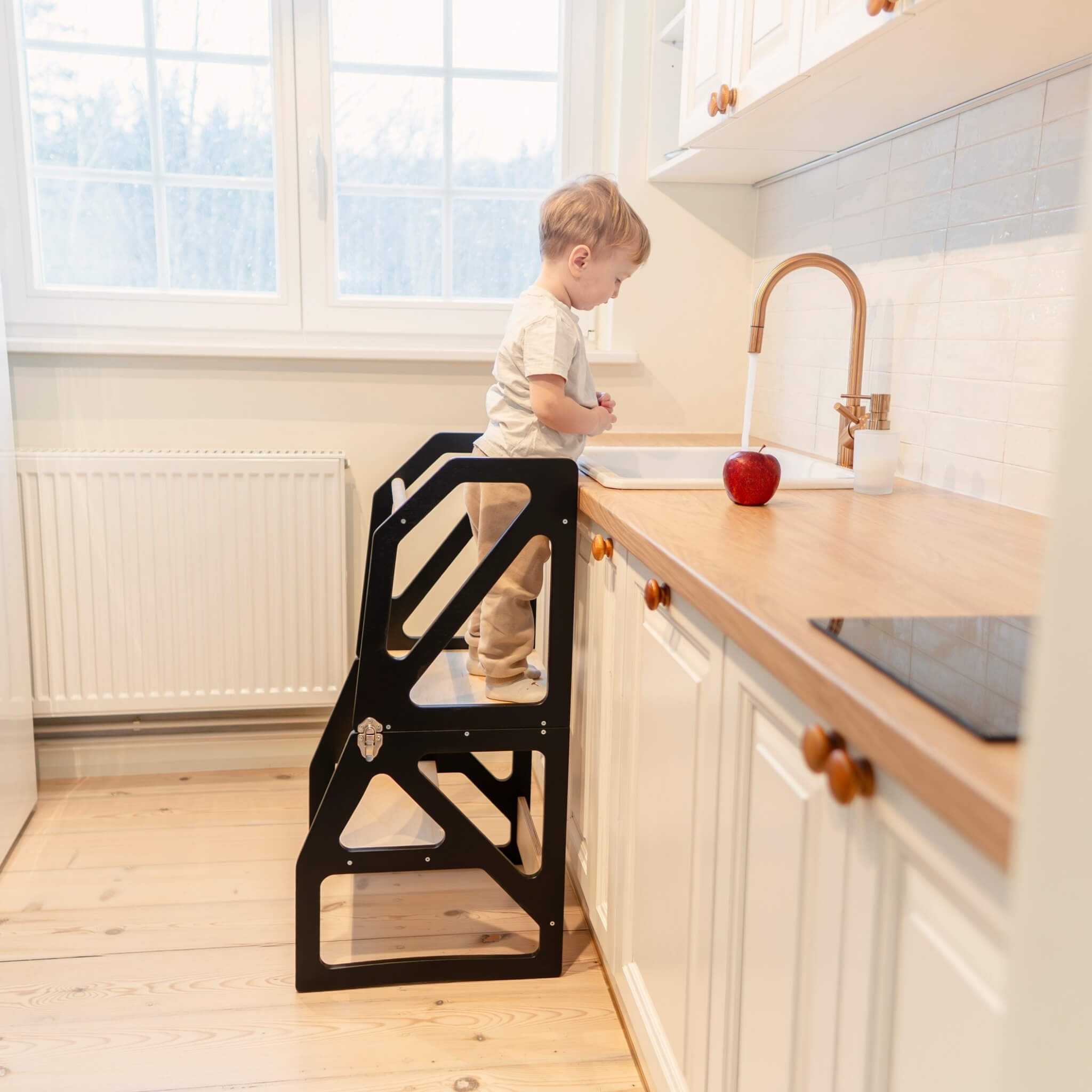 Child using black transformable kitchen tower at kitchen counter, adjustable wooden helper tower